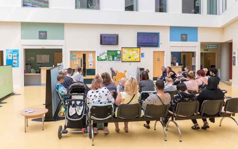 People sitting in a hospital waiting room looking at a digital signage queue management system